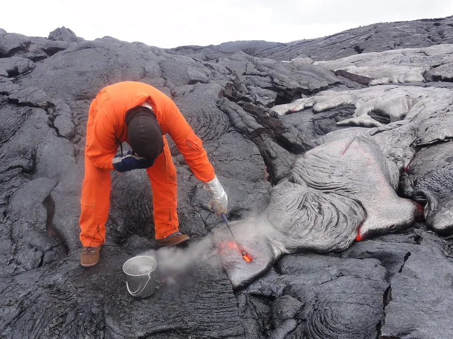 A scientist in a silver heat-proof suit studying glowing lava up close
